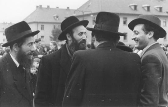 Eine Gruppe religiöser jüdischer Männer unterhält sich draußen vor dem Displaced Persons Camp Bergen Belsen (1).jpg